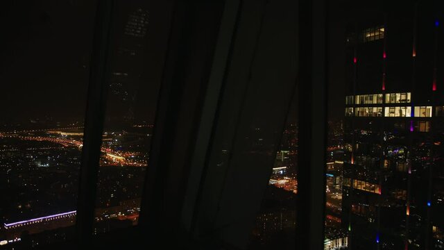 Panoramic night cityscape view on Moscow City with MSU Moscow Stat University building from the high skyscraper through the window glass. Slow motion dolly shot