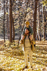 Fototapeta premium Caucasian Little boy and father walking in the autumn park on autumn, man holding son on shoulders. adult male and little kid boy enjpy holidays together, weekends outdoors. portrait