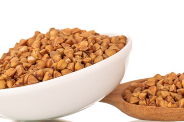 Uncooked organic buckwheat groats in a white ceramic saucer with a wooden spoon, close-up, isolated on white.