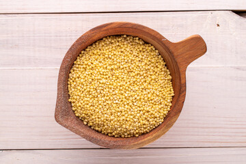 Uncooked organic millet groats in a wooden cup on a wooden table, macro, top view.