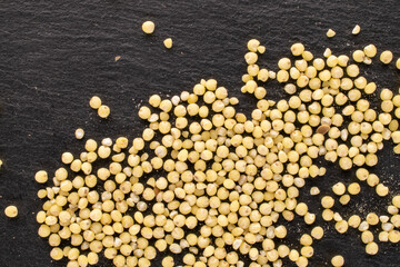 Uncooked organic millet groats on a slate stone, macro, top view.