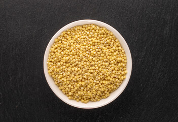 Uncooked organic millet groats in a white saucer on a slate stone, macro, top view.