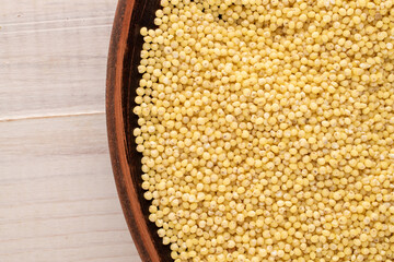 Uncooked organic millet groats with a clay dish  on a wooden table, macro, top view.