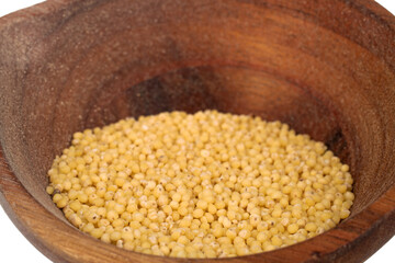 Uncooked organic millet groats with wooden cup, close-up.