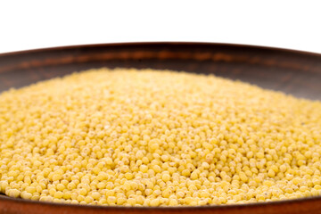 Uncooked organic millet groats on a clay dish, close-up, isolated on white.