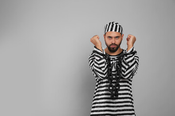 Prisoner in special uniform with chained hands on grey background, space for text