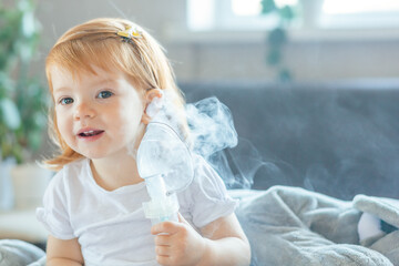 portrait toddler girl holds a mask from a nebulizer in her hand and smiles sitting at home. 