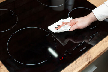 A young woman is cleaning an induction electric hob. Cleaning in the kitchen. Electric oven...