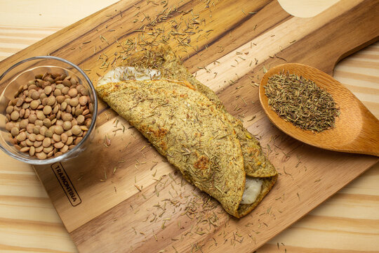 Uma panqueca de lentilha, com um copo de lentilhas cruas e uma colher cheia com tomilho. Tomilho salpicado sobre uma t&aacute;bua de madeira.
