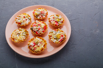 Salad with crab in tartlets on a beige plate on a black background.