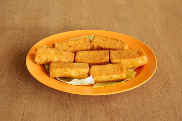 Fried crispy tofu in orange dish isolated in wood table background top view