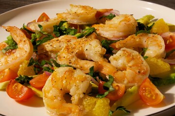 Bright salad in a white plate on the loft table with shrimp, red tomatoes and herbs.