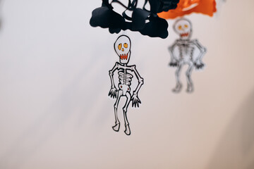 paper skeletons garland on white wall. Halloween background, Copy space for your text. Selective focus.