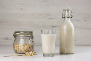 Dairy free oat milk and flakes in a glass jar on light background