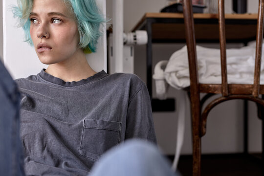 Unhappy sad worried young woman in casual wear sit on bedroom floor alone troubled with loneliness, upset about solitude mental problem look at window think of bad mistake, biting lips