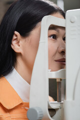 asian woman checking vision on blurred autorefractor.