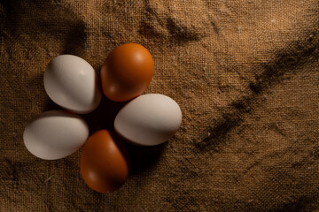 Five eggs, white and brown, lie on the burlap. Five eggs close-up shot from above. Farm, organic chicken eggs, on a textured burlap backing.