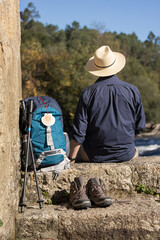 View from behind of a male pilgrim resting and on his way to Santiago de Compostela with his backpack and accessories for the journey. Camino de Santiago - obrazy, fototapety, plakaty
