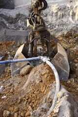 Greifer eines Baggers gräbt sich neben einem Kabel in den Boden