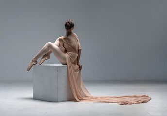 Ballerina dancing on ballet pointe shoes in body color leotard and long cloth in a white studio
