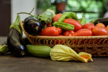 Woven basket on a wooden table filled with ripe organic tomatoes and other vegetables.