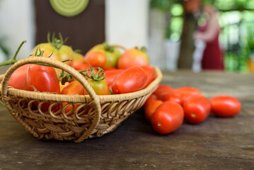 Woven basket on a wooden table filled with ripe red organic tomatoes.