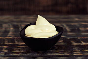 Mayonnaise in a black bowl. Homemade mayonnaise on a black old table. Black bowl with sauce on a background of dark wooden boards.
