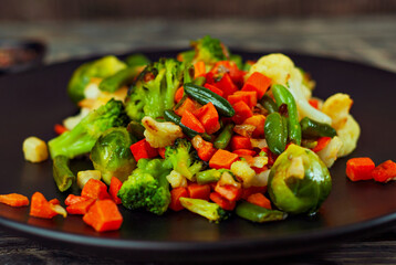 Mix of vegetables close up. Salad of various chopped vegetables. Roasted cabbage, carrots, broccoli, peas in a black plate. Food on the background of an old wooden board.