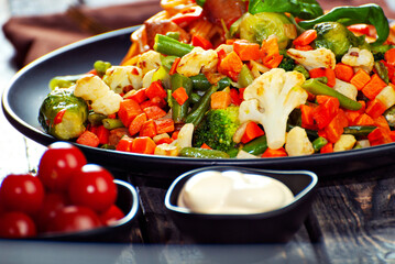 Noodles with carrots, vegetables and meat in a black plate. Food on a black Yerevan table. Basil leaves on pasta. Pasta with a mixture of vegetables. Pickled tomatoes and spices in the background.