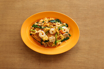 Chinese Fried Mee Sua in orange plate on wooden table top view seafood
