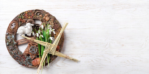 Wiccan altar for Imbolc sabbat. pagan festive ritual. Brigid's cross amulet of straw, wheel of the year, snowdrops, toy lamb on wooden table. Imbolc holiday, spring equinox. flat lay. copy space - obrazy, fototapety, plakaty