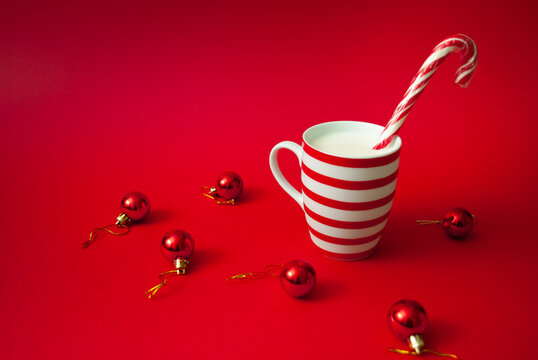 Red Christmas Candy Cane in colorful mug of milk with red Christmas boubles on red background.
