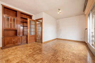 Empty living room with wooden bookcase embedded in a wall, bay window and oak parquet floors