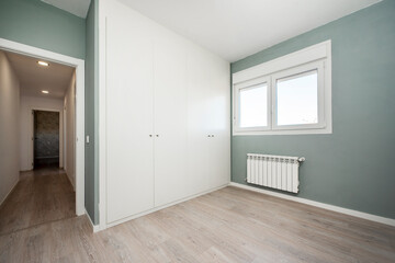 Room with one wall painted in light green and another covered with a large white built-in wardrobe