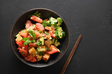 Chinese crispy spicy fry eggplant with cucumber, garlic, tomatoes, fresh cilantro leaves in oyster sauce and black vinegar on black background. View from above. Copy space.