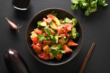 Chinese crispy spicy eggplant with cucumber, garlic, tomatoes in oyster sauce and black vinegar on black background. Chinese appetizer and Asian food. Top view. Flat lay.