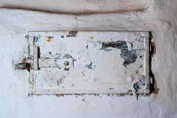A very old metal view door of a stone rustic stove. There are traces of rust and a loose layer of paint. Close-up. Background.
