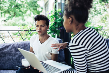 Skilled diverse colleagues discussing web project and graphic design during collaborative brainstorming meeting in street cafe, multiracial male and female IT professionals working remotely together