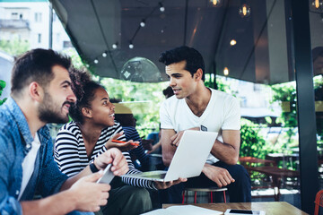 Multiracial remote colleagues cooperating on project ideas discussing graphic design during brainstorming meeting in street cafe young millennial students 20s e learning on laptop technology