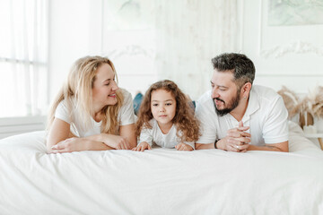 Happy young family. Man, woman and daughter on the sofa. Light background, studio shot. Interracial marriage, different nationalities