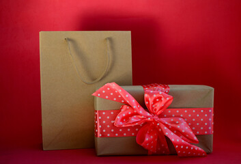 Gift box with red bow and craft shopping bag on red background with copy space. Gift for Valentine's Day, March 8, mother's day, black friday, birthday.