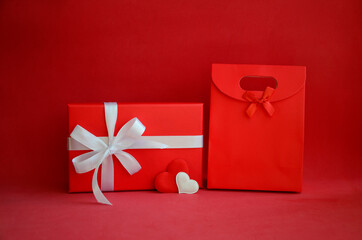 Red gift box with white bow, shopping bag and hearts on red background with copy space. Gift for...
