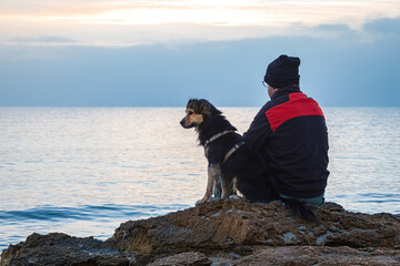 A man and a dog sitting on a rock by the sea