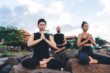 Men and woman enjoying yoga during morning breathing in asana training body shape, inspired people sitting in Lotus pose keeping mental and physical strength during yoga namaste concentration