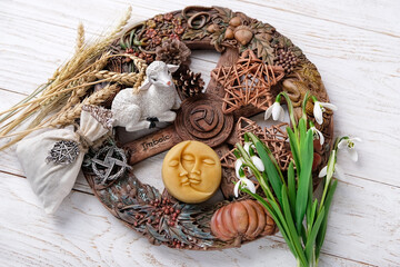 Wiccan altar for Imbolc sabbat. pagan festive ritual. Brigid's cross amulet, sun-moon symbol, wheel of the year, snowdrops, toy lamb on wooden table. Imbolc holiday, spring equinox. top view. close up - obrazy, fototapety, plakaty