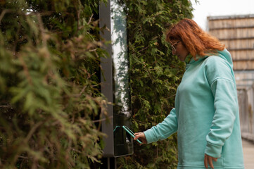 A woman uses a street self-service terminal for contactless payment with a smartphone.