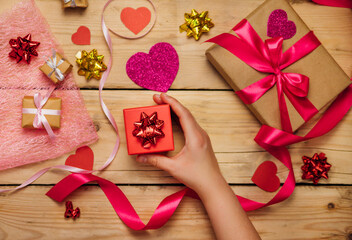 Women's hands hold a red gift box on a wooden background. The concept of Valentine's Day, Mother's Day.