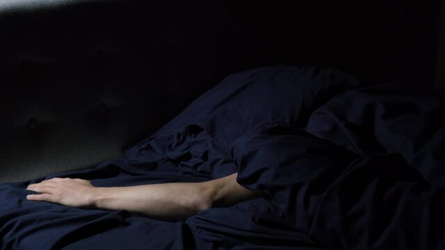 Disturbed sleep. The young guy tosses and turns in bed. Covers his head with a pillow so as not to hear the noise