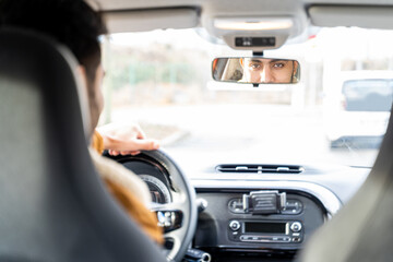 Caucasian or eastern ethnicity man casually dressed with hands holding driving wheel, looking in rearview mirror smiling in car on sunny day. Travel, trip, holiday, exam, lesson, learning, taxi driver