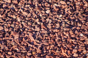 Red decorative granite crushed stone of a small fraction, a background on the theme of building materials with a depth of field. Bulk material road surface